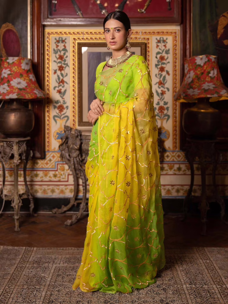 This is a woman donning a yellow chiffon saree with green hues for Durga Puja 2025