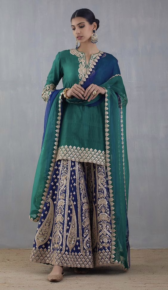 Woman wearing a green kurta with a heavily embroidered lehenga and dupatta, showcasing festive ethnic wear essentials India for weddings and traditional occasions