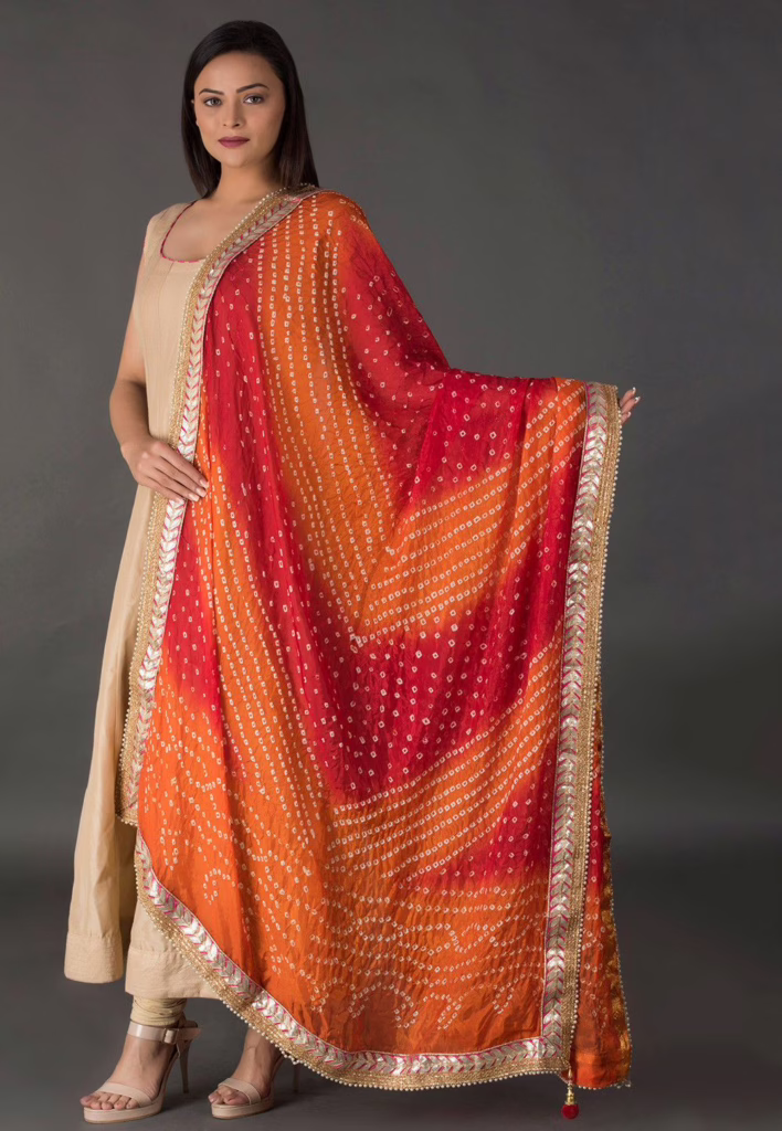 Woman wearing a beige kurta with a vibrant bandhani dupatta in red and orange, highlighting ethnic wear essentials India and traditional dupatta styles