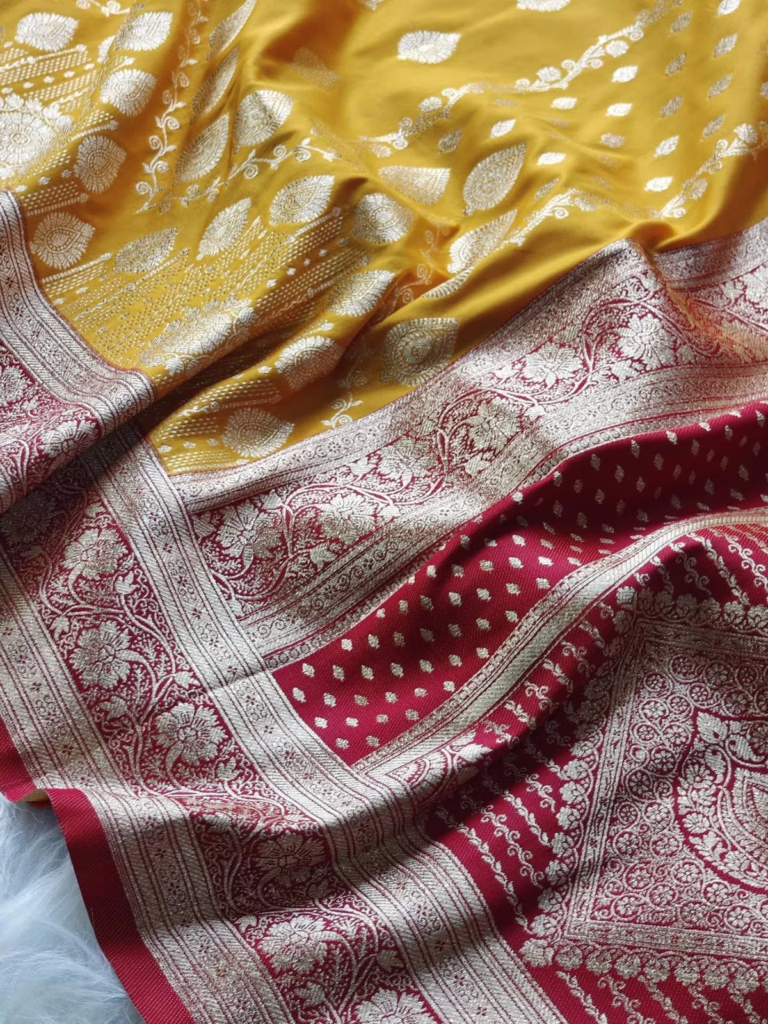 Close-up of a yellow and red Banarasi silk saree featuring intricate silver zari floral and paisley motifs with a richly woven border.
