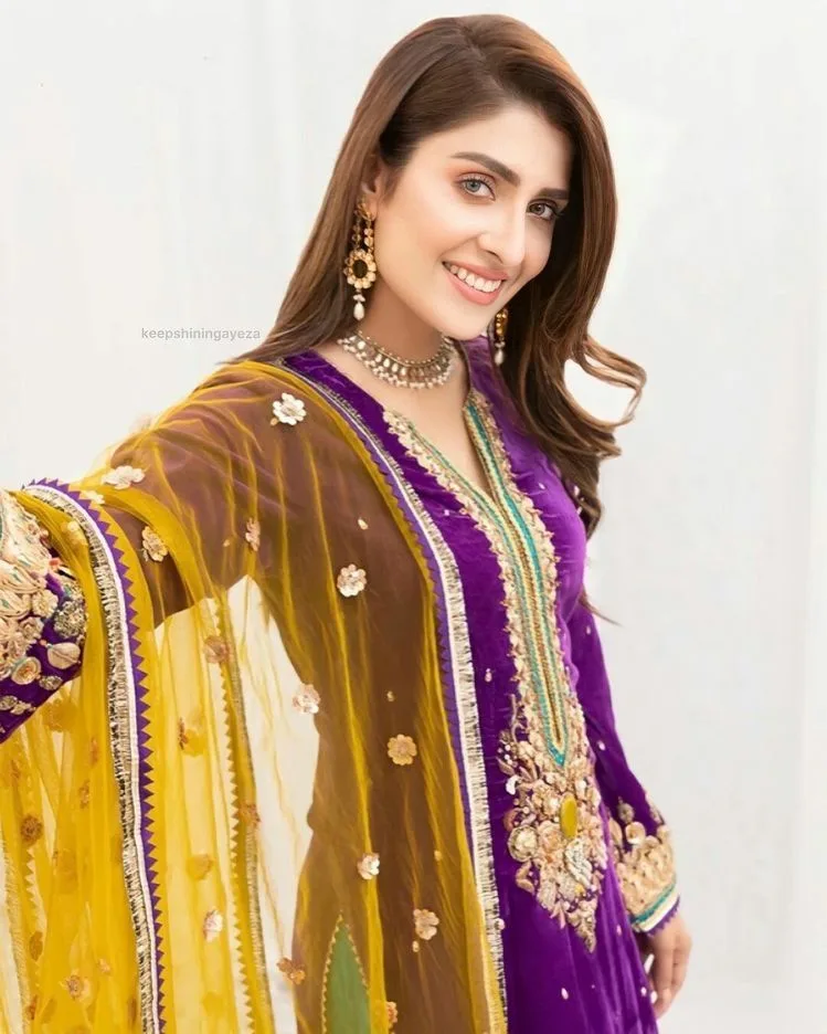 Woman wearing a royal purple embroidered ethnic suit with a mustard yellow sheer dupatta featuring floral embellishments and an embroidered border.
