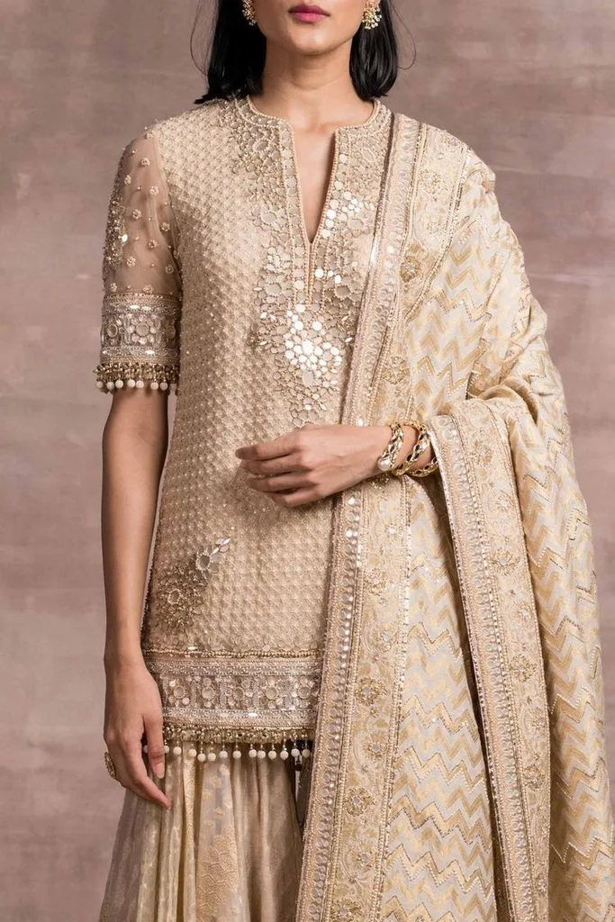 Elegant woman wearing a cream and gold heavily embroidered kurta with matching palazzo pants and a patterned embellished dupatta.