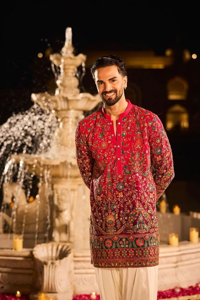 This is an image of a man wearing a vibrant orange Kurta smiling into the camera amidst a festive backdrop.